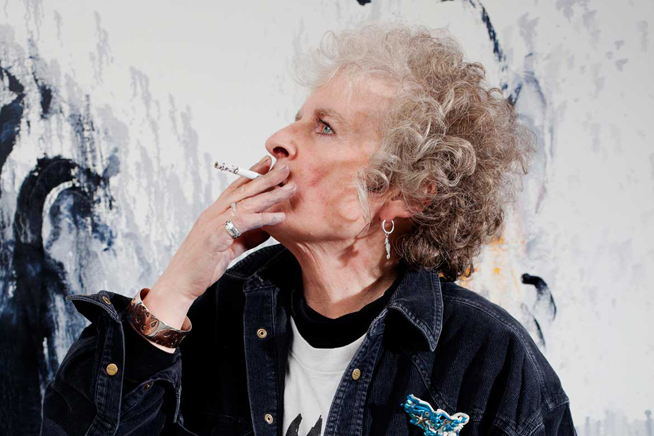 A photo of Maggi Hambling smoking in front of her painting